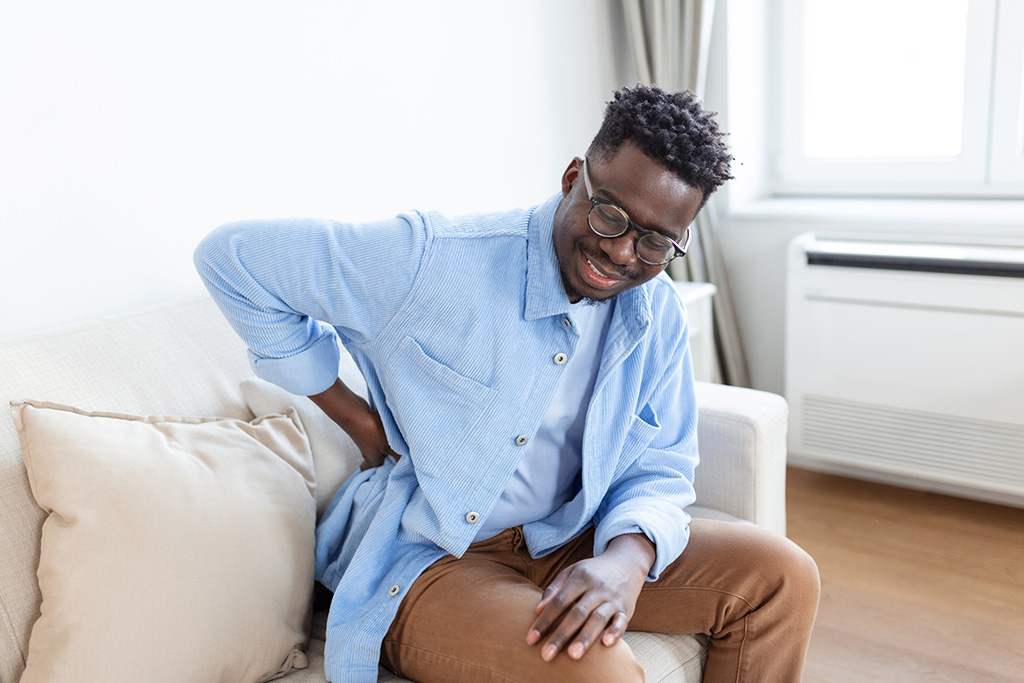 Unhappy Man suffering from backache at home. Lower Back Pain . Man feels back pain massaging aching muscles, sad man suffers from low-back