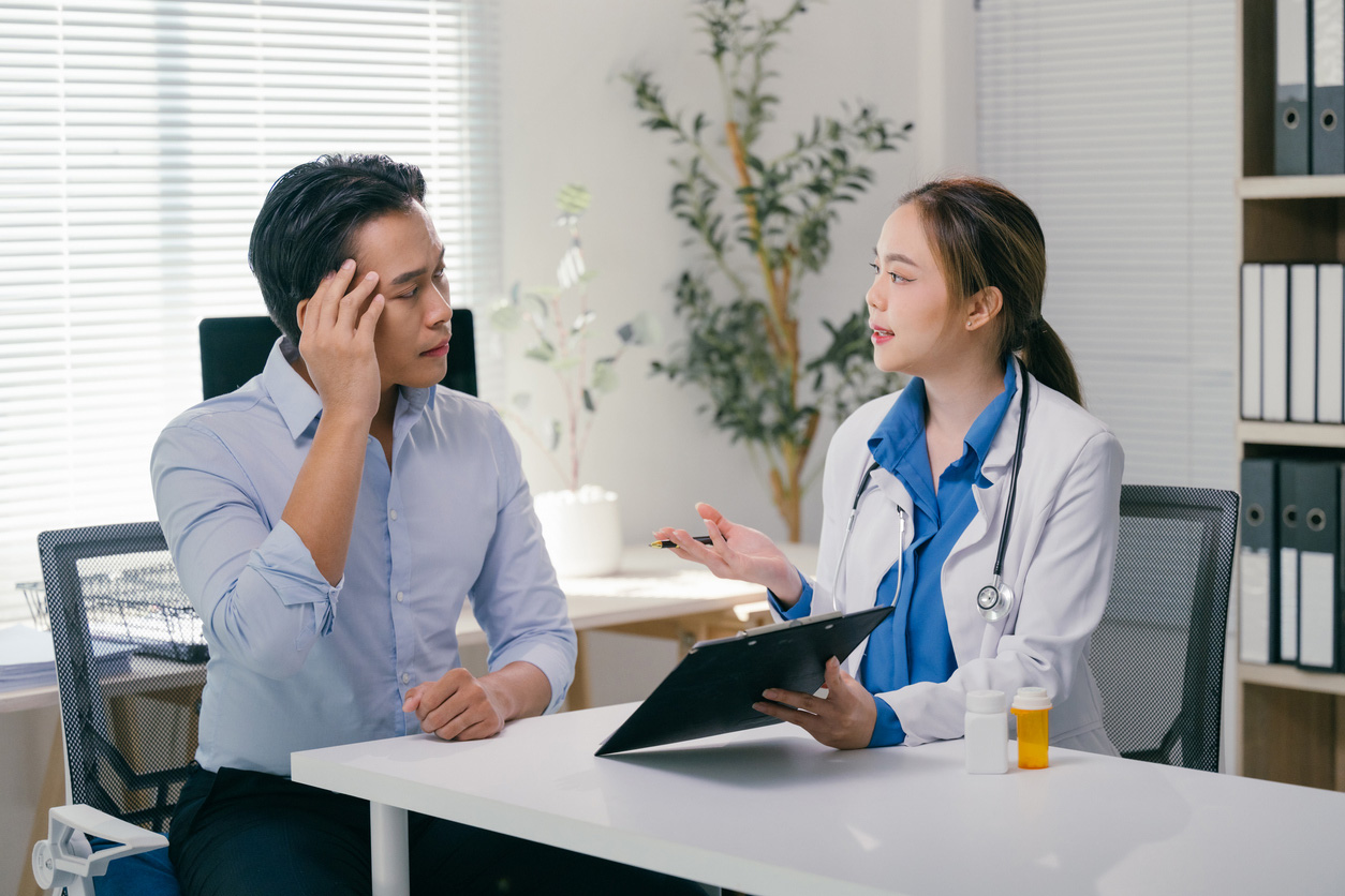 Female doctor holding clipboard listening to patient complaints about headache, offering diagnosis and prescribing medication during medical consultation in clinic office