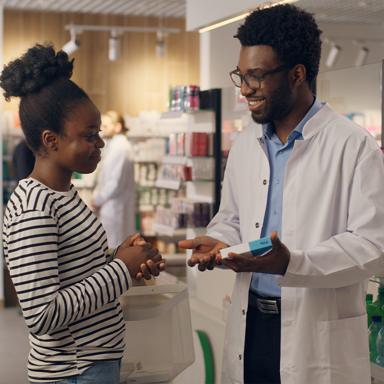 Young pharmacist talking to male customer in a drugstore. Focus is on customer.