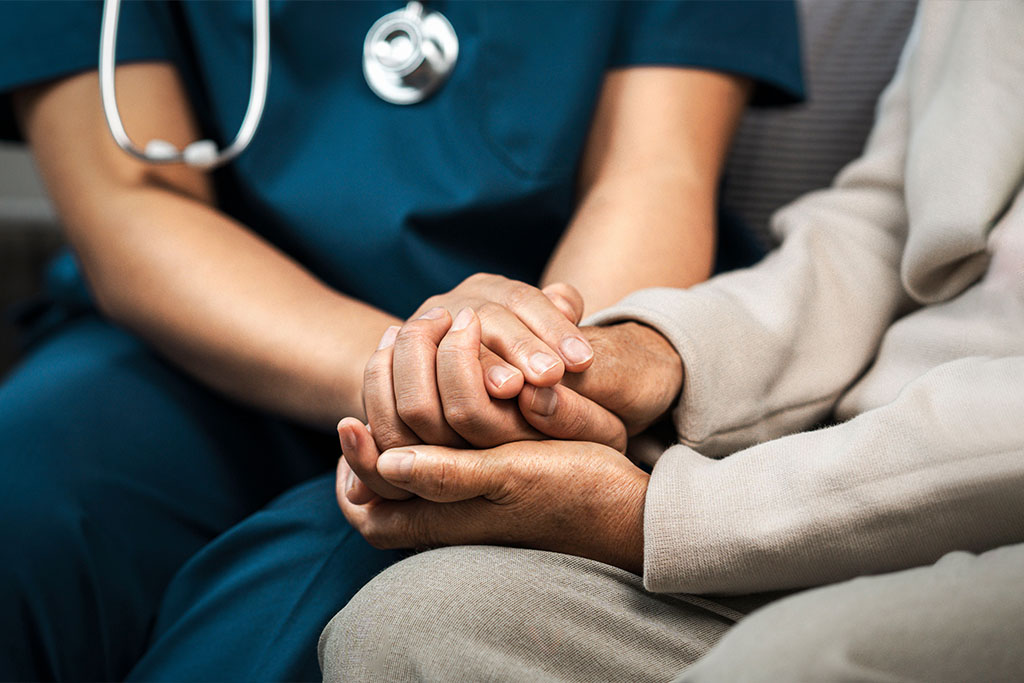A medical professional holding the hands of their patient, to provide reassurance and peace.