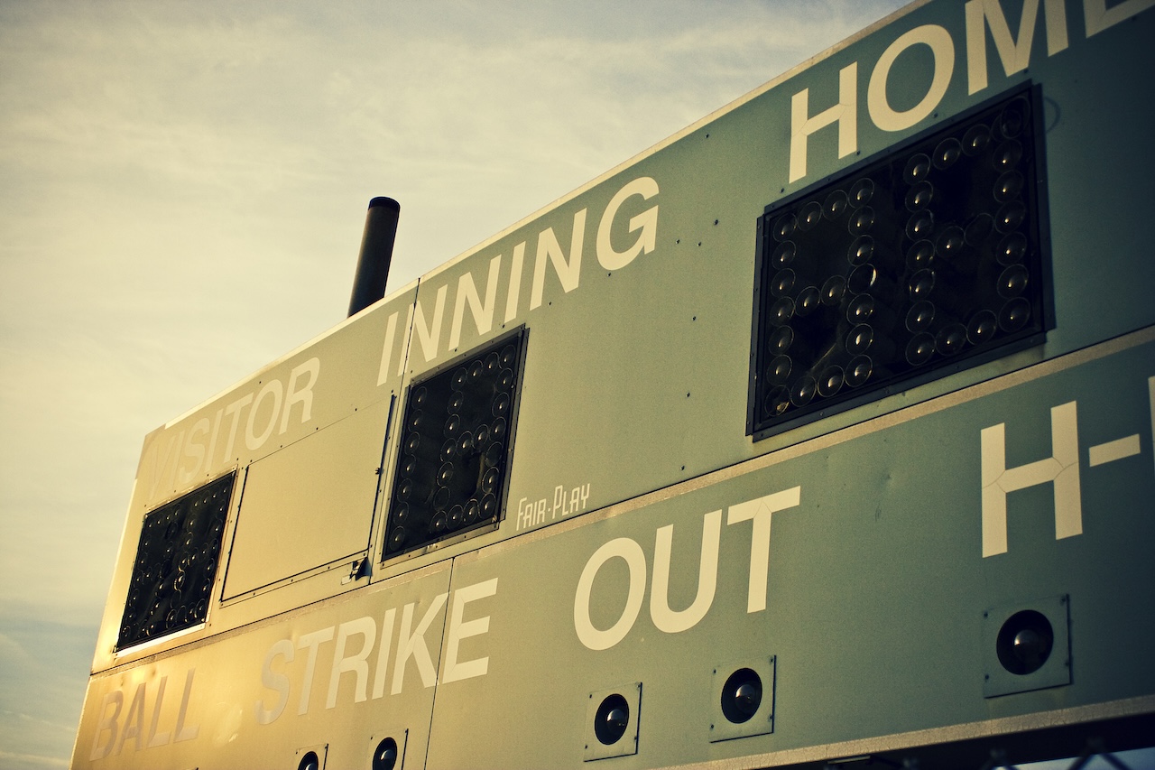 An angled photo of a baseball scoreboard, reflecting late afternoon sun.