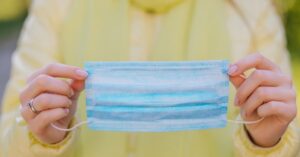 A woman holding a blue disposable medical face mask to prevent the spread of contagious viruses and flu, illustrating preventive health at AllCare.