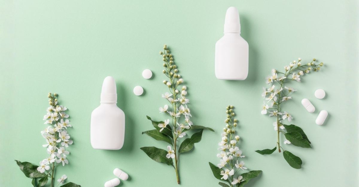 A nasal spray bottle positioned next to blooming spring tree branches, representing seasonal allergy relief and treatment at AllCare.